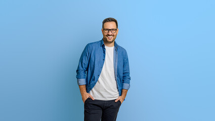 Portrait of smiling male entrepreneur with hands in pockets standing confidently on blue background