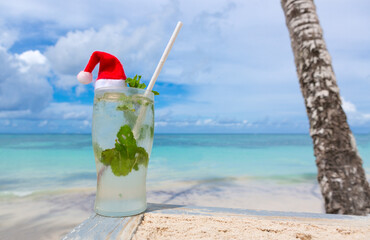 Christmas background with drinks Bocal with Santa hat on Caribbean beach.