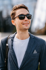 Close up crop portrait of a handsome young man wearing jacket and sunglasses outdoors.