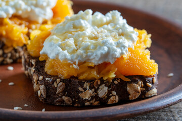 Bread slices with cheese, stewed pumpkin pulp, honey on wooden board. Delicious breakfast on...