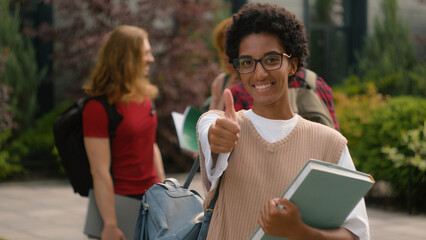 Students talking near university campus outdoors African American happy satisfied student girl woman showing thumb up like recommend gesture after class education with book good high school knowledge