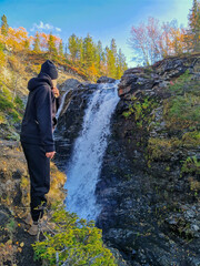 A girl on the background of a beautiful waterfall in the autumn mountains beyond the Arctic Circle...