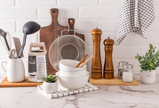 different kitchen utensils and tools made of natural materials on a light stone countertop and plants in pots front view. Eco-friendly cuisine.
