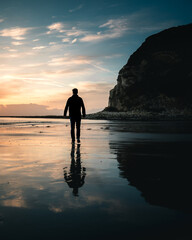 Silhouette of a man walking on wet sand at sunrise