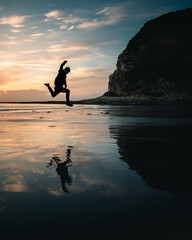 A man jumping at a beach sunrise as the wet sand reflects back