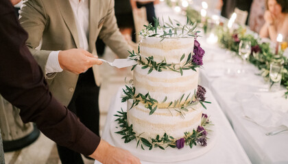 Men take a piece of wedding cake on the table with a spatula. Cropped. Faceless