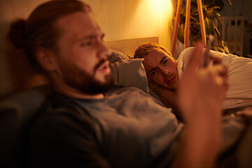 disloyal gay man browsing date app on smartphone near discouraged boyfriend at night in bedroom - obrazy, fototapety, plakaty
