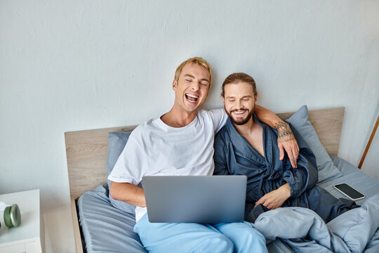 Cheerful Gay Couple Watching Movie On Laptop And Laughing On Bed, Happy Love And Relationships