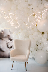 Arch decorated white balloons, angel wings, bears and chair for baptism. Photo area decoration space with white background. Trendy decor. Celebration concept. Reception at birthday baby party on wall.