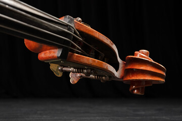 Beautiful classic brown double bass neck, double bass scroll and tuning pegs on a black background, music concept. Shallow depth of field