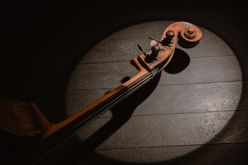 Violin in the dark. Ancient brown contrabass neck in a circle light on a black floor of stage,...