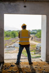 Young Asian civil engineer or construction supervisor wearing a helmet looks away and smiles while inspecting a construction site.