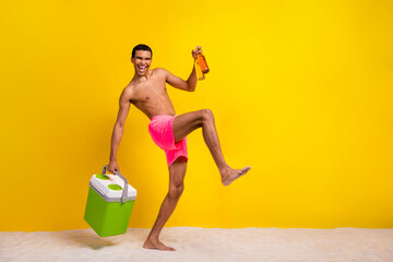 Full length photo of funny excited shirtless man holding refrigerator inviting drink beer empty space isolated yellow color background - obrazy, fototapety, plakaty