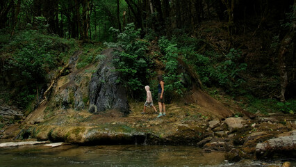 Mother and boy walking along the river and giant stones. Creative. Green dense forest on the...