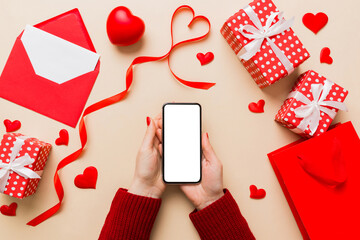 Woman hand holding mobile phone with blank screen on colored background with hearts, valentine day concept top view flat lay