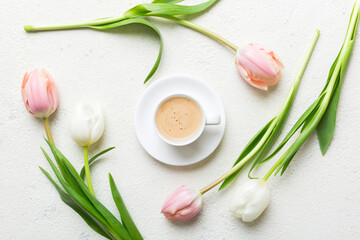 Obraz na płótnie Canvas Spring background with flowers, a cup of coffee and a bouquet of pink and white tulips on colored table background with place for text. Copy space top view