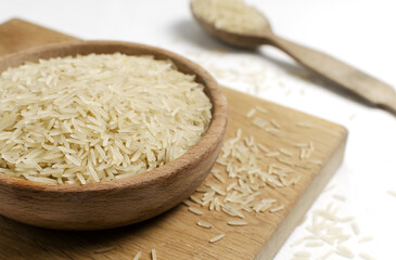 Raw basmati rice in a wooden bowl with a spoon on a cutting board. Concept of Water-Conserving Products. Saving water. Horizontal orientation. Selective focus.