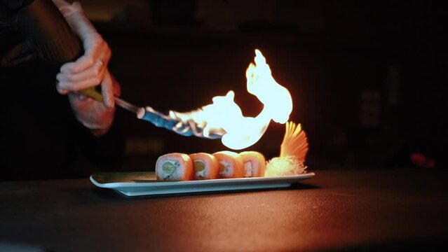 Master sushi maker makes sushi rolls from nori rice and red fish, the process of preparing Japanese food close-up, orange salmon trout fish, scorched by fire