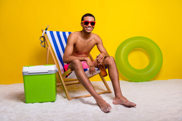 Full length photo of good mood positive shirtless man having rest lounge chair drinking beer isolated yellow color background