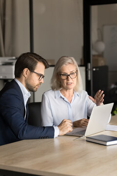 Confident Younger And Older Business Colleagues Couple Analyzing Online Project Content, Speaking At Laptop, Working Together, Talking On Video Conference Call. Vertical Shot