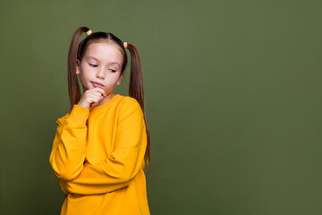 Portrait of confused cute small kid with tails dressed yellow sweatshirt look down at empty space isolated on khaki color background