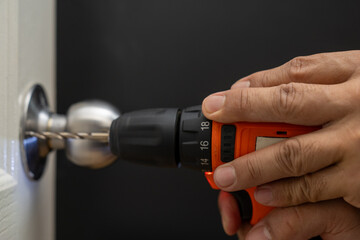 Asian professional locksmith installing or repairing a door knob with screw drive or cordless...