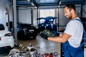 Happy arabian male auto mechanic or car repairman holds Electronic Control Unit (ECU) of modern...