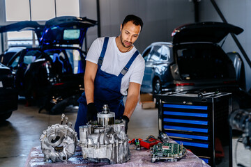 Electric car engine removed from car for repair. Arabian man use voltmeter working Internal...