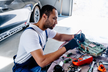 Arabian male auto mechanic examining a car engine removed from car for repair with voltmeter....