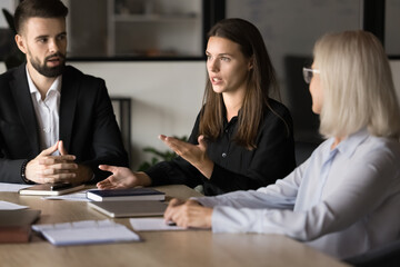 Serious pretty young project manager talking to coworkers on brainstorming meeting, offering...