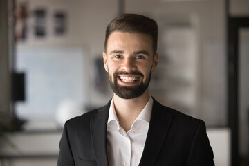 Fototapeta premium Happy handsome young businessman in formal suit looking at camera with toothy smile, laughing. Business leader man, company executive professional head shot video call portrait