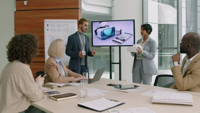 Marketing team with two project leaders standing in well-lit meeting room brainstorming ideas of better promotion of new VR set