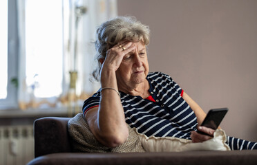 Elderly woman sitting on couch and using mobile phone at home
