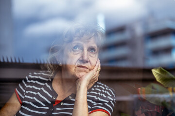 Portrait of senior woman looking through window 
 - obrazy, fototapety, plakaty