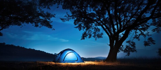 Blue camping tent illuminated by sunlight with trees silhouette outdoors