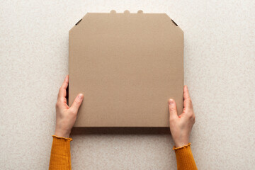 Pizza closed carton box in caucasian hands on kitchen table flat lay mockup with copy space