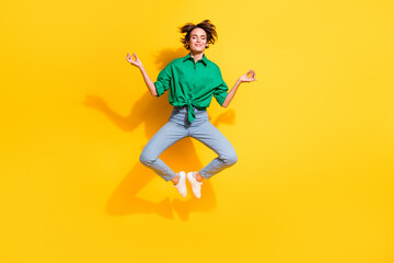 Full length photo of sweet dreamy lady wear green shirt jumping high closed eyes enjoying yoga isolated yellow color background
