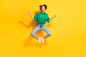 Fototapeta premium Full length photo of sweet dreamy lady wear green shirt jumping high closed eyes enjoying yoga isolated yellow color background