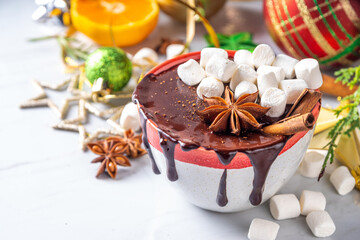 Winter aromatic hot chocolate cup with Christmas background. Mug of dark hot cocoa drink with cinnamon, anise, spices and marshmallow, on cozy Christmas and New Year holiday decorated background 