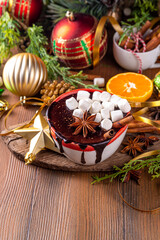 Winter aromatic hot chocolate cup with Christmas background. Mug of dark hot cocoa drink with cinnamon, anise, spices and marshmallow, on cozy Christmas and New Year holiday decorated background 
