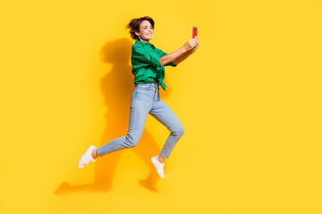Fototapeta na wymiar Full length photo of excited pretty girl dressed green shirt jumping chatting modern device isolated yellow color background