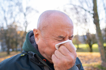 runny nose in adult, elderly man blowing nose into tissue while on walk, Outdoor activities for...