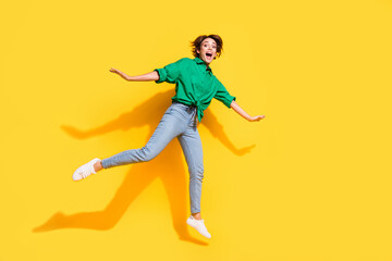 Fototapeta na wymiar Full length photo of excited funky girl dressed green shirt jumping high empty space isolated yellow color background