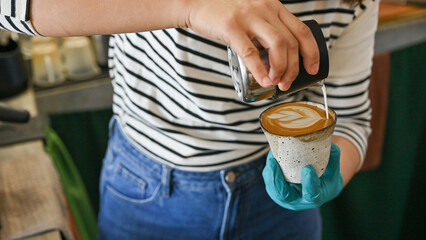 Female barista pouring steamed milk to hot coffee to making latte art. A latte is a coffee drink...