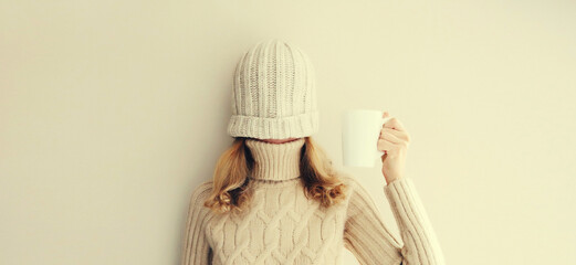 Cheerful funny woman having fun, pulling winter hat over her face warm up holding cup of hot coffee...