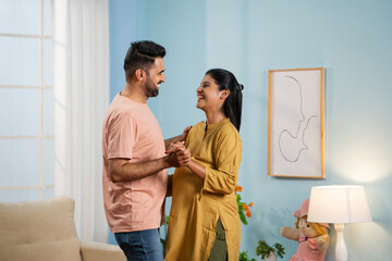 Joyful Indian Pregnant wife with Husband doing romantic dance at home - concept of affectionate,...