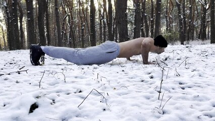 Strong man doing push ups on snow at winter forest. Sportsman exercising at nature. Young guy training outdoor. Muscular athlete showing hard and intense workout. Concept of sportive lifestyle
