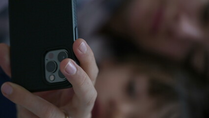 Close-up of mother and child looking at cellphone device screen laid in bed. Parent and son...