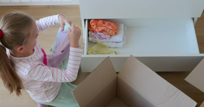 Little girl putting clothes to drawer in bedroom after moving
