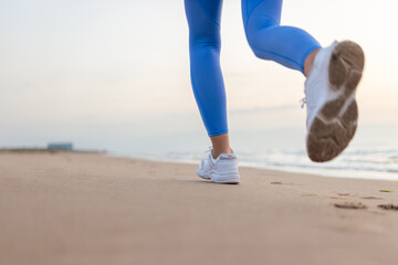 legs a girl in blue leggings and sneakers running along the beach at dawn with space for inscription